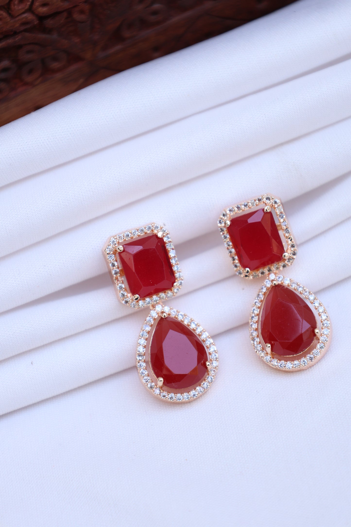 Pair of earrings with red gemstones and gold accents on a white background