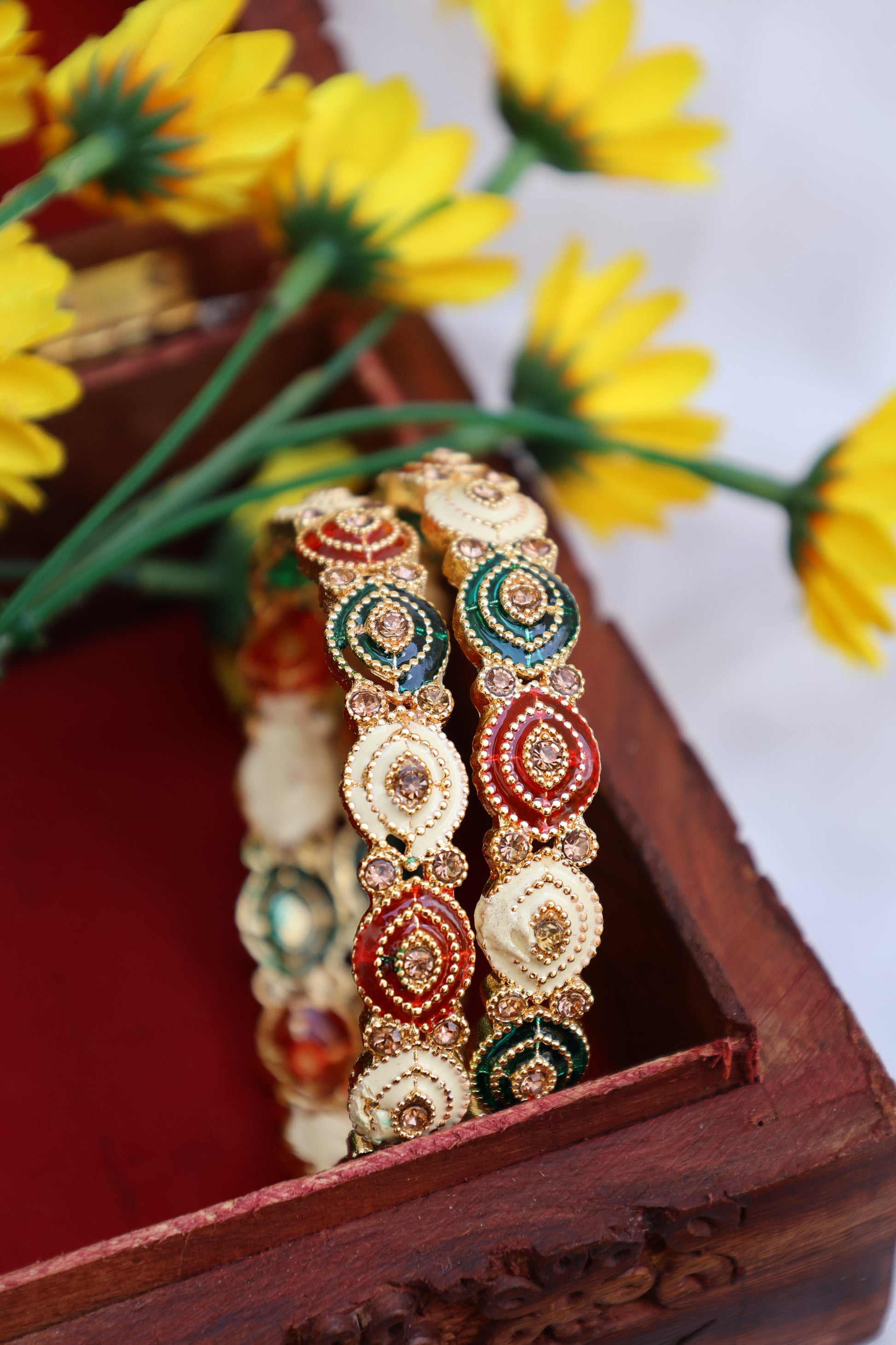Decorative bangles with intricate designs on a wooden stand with yellow flowers in the background.