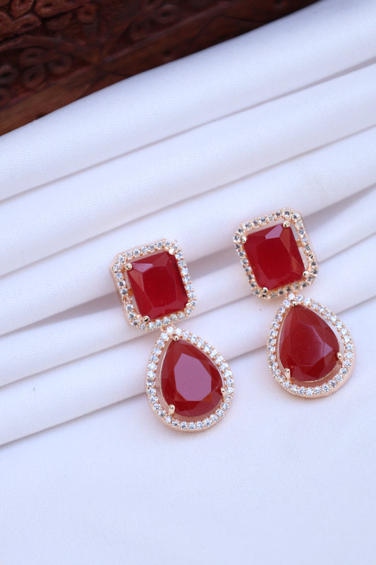 Pair of earrings with red gemstones and gold accents on a white background